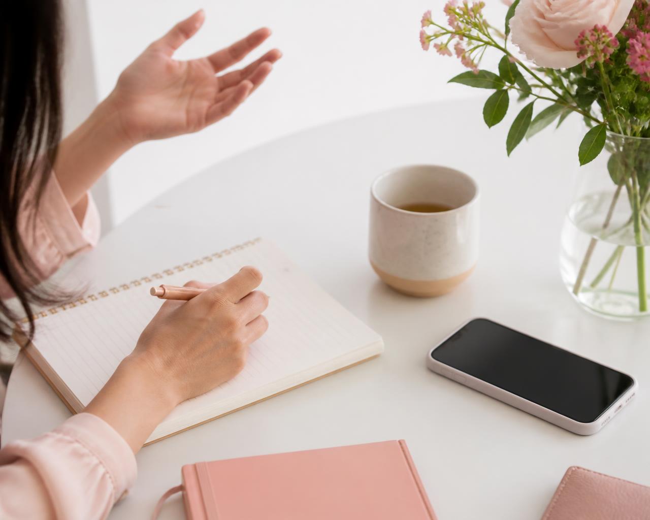 A consultant taking notes at a bright desk with a phone and tea, mid-conversation with a client.